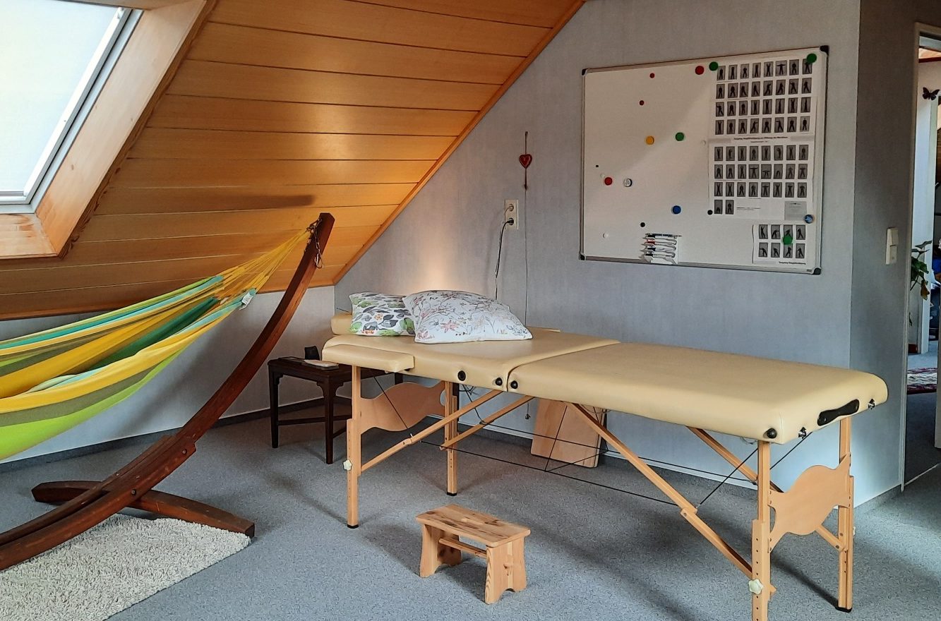 Behandlungsraum mit Massagetisch, Hängematte und einem Flipchart an der Wand.